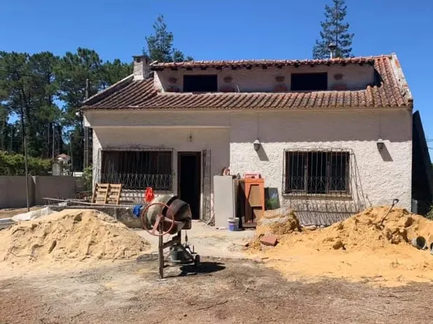 Moradia de um piso com sótão antes da ampliação, com areia e betoneira à frente.