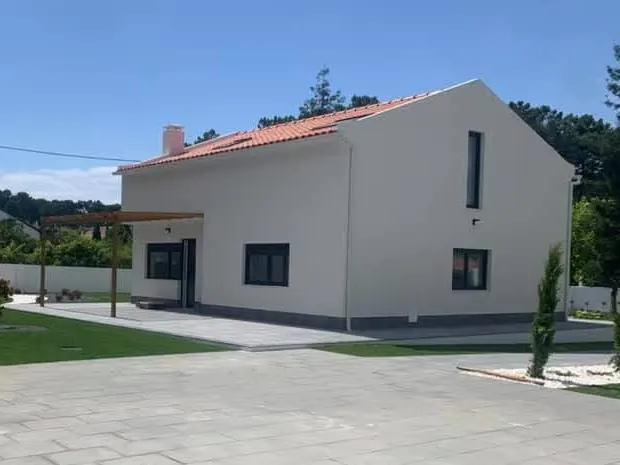 Moradia depois da ampliação, com dois pisos, cobertura nova, pérgola de madeira e pátio em lajeta.