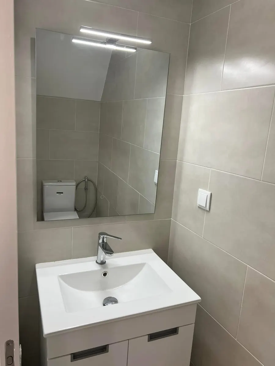 Depois da obra: lavatório com móvel branco e espelho com luz, em parede de cerâmica cinza-bege.