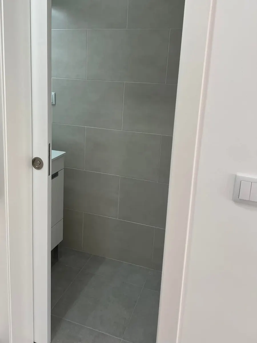 Depois da obra: porta de correr embutida aberta para a casa de banho com chão cinzento.