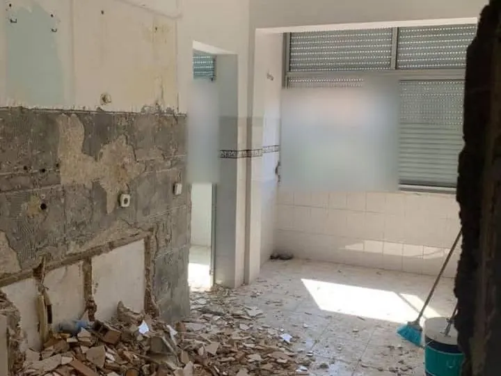 Antes: cozinha em demolição, com paredes sem azulejo, entulho no chão e janela ao fundo.