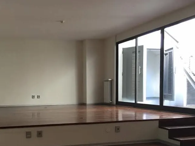 Sala vazia antes da obra, com estrado de madeira e envidraçado virado para o pátio.