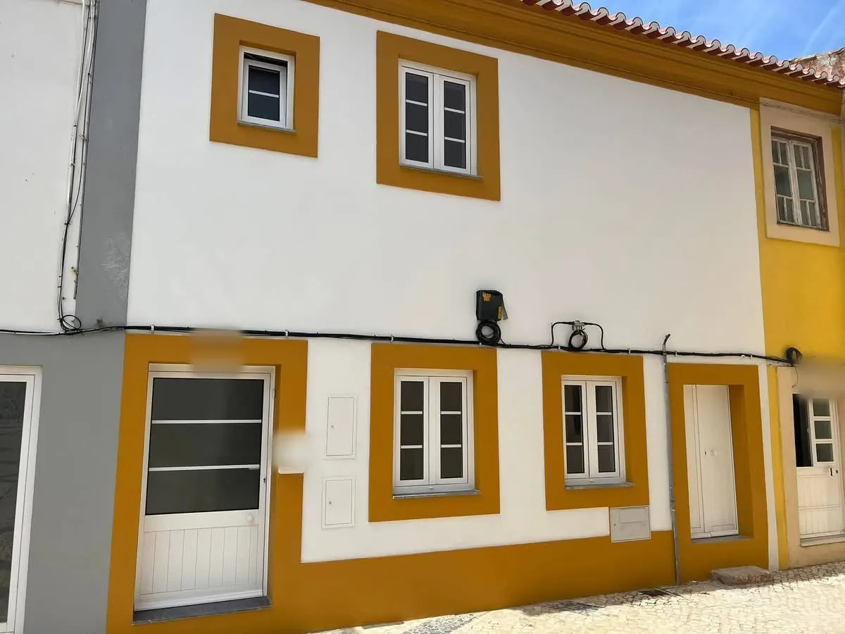 Depois da obra: fachada de dois pisos pintada de branco, com molduras cor de mostarda.